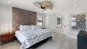 Ein Schlafzimmer mit Bett, Nachttisch, Deckenventilator, Kunstwerk und einer Tür.