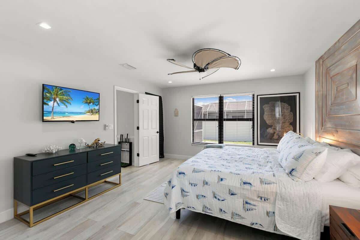 A bedroom with a bed, a dresser, a ceiling fan, a window with blinds, and a painting on the wall.