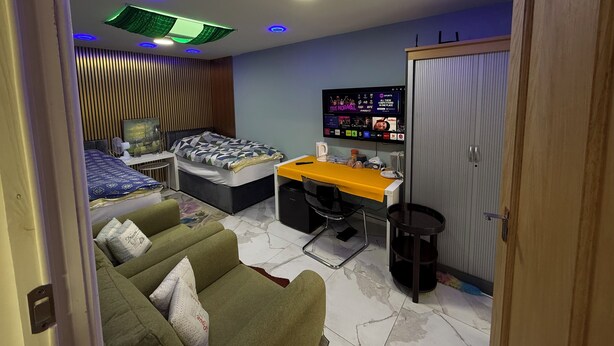 A modern bedroom with a bed, a desk, a TV, and a sofa.