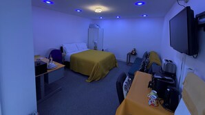 A hotel room with a bed, a desk, a chair, a table, a TV, a coffee maker, and a wardrobe.