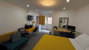 A hotel room with a bed, a desk with a computer, a television, and a sofa.