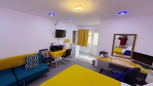 A hotel room with a bed, a desk with a computer, a chair, a sofa, a TV, and a mirror.