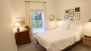 Un dormitorio con una cama grande, un aparador de madera, una mesita de noche, una ventana con cortinas e iluminación en la pared.