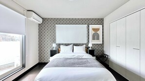 Ein modernes Hotelzimmer mit einem großen Bett, einem Nachttisch, einer Wandlampe und einem Kleiderschrank.