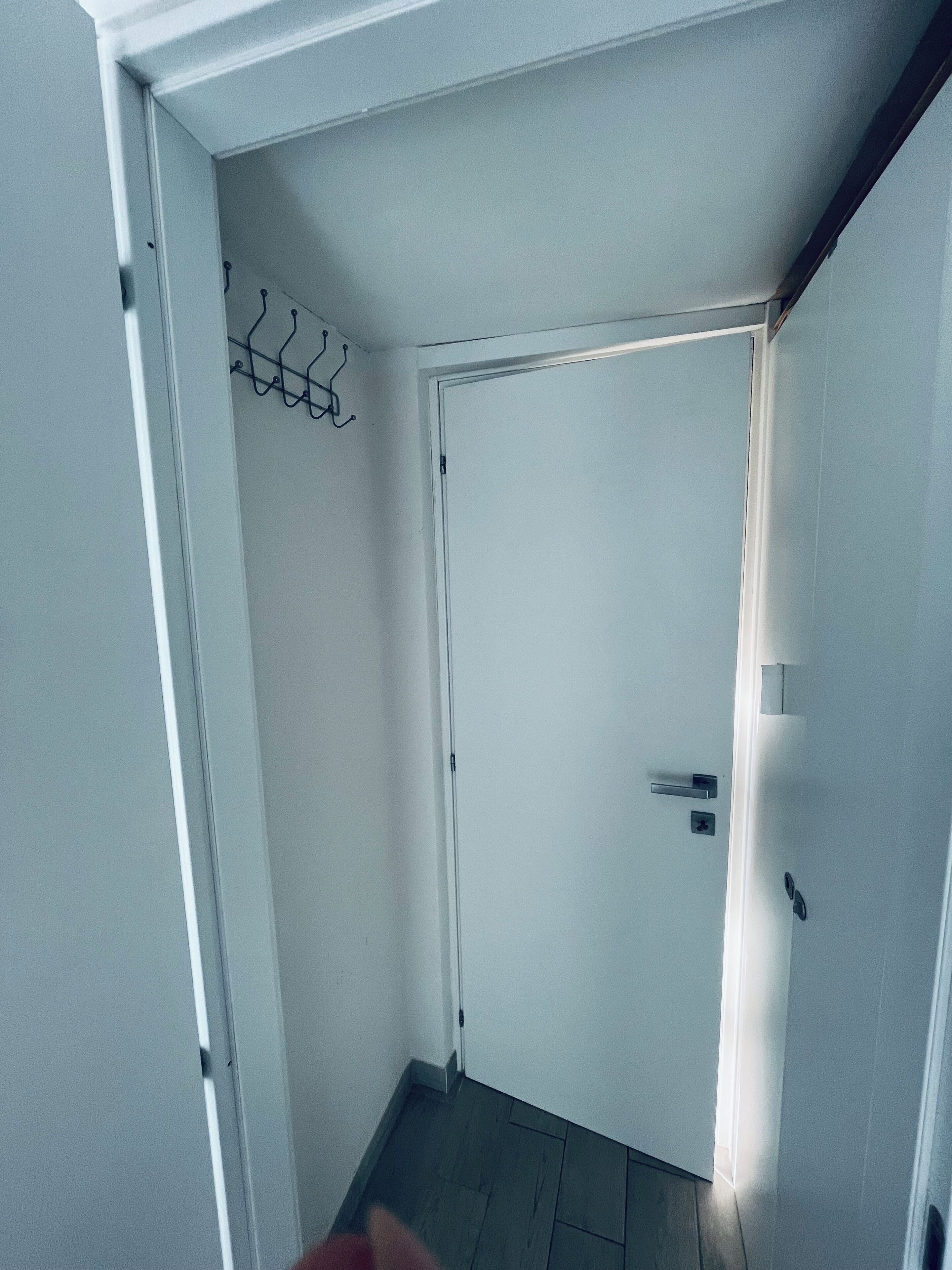 Ein schmaler Flur mit einer weißen Tür, einem Kleiderständer und einem kleinen Fenster.