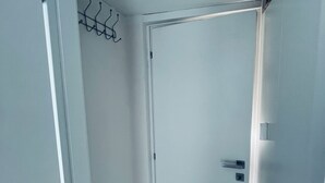 Ein schmaler Flur mit einer weißen Tür, einem Kleiderständer und einem kleinen Fenster.