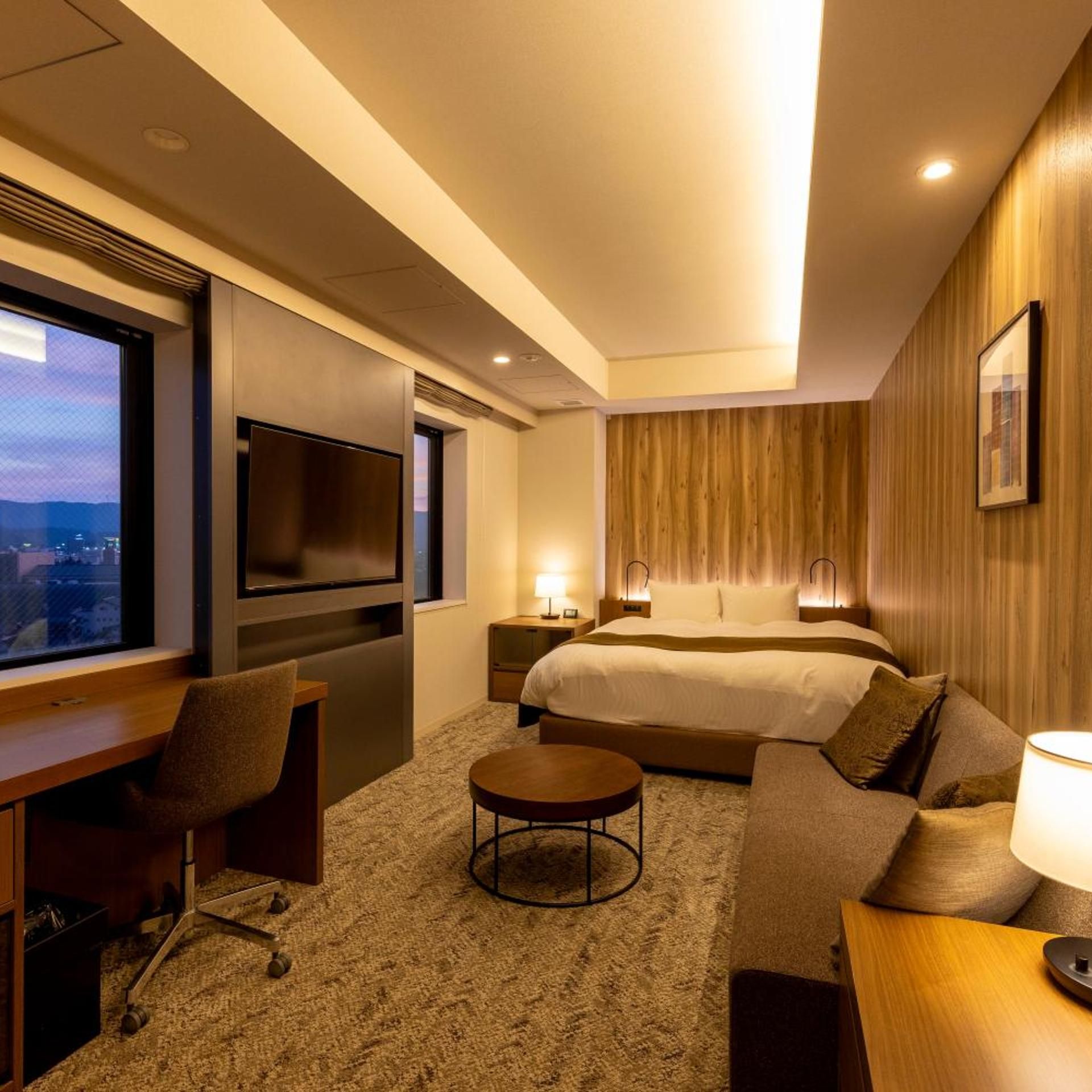 Una habitación de hotel con cama, escritorio, silla, una mesa redonda para café y televisor.