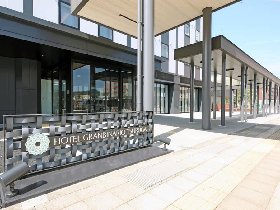 A modern hotel entrance with a clear sign, a covered walkway, and a parking area.