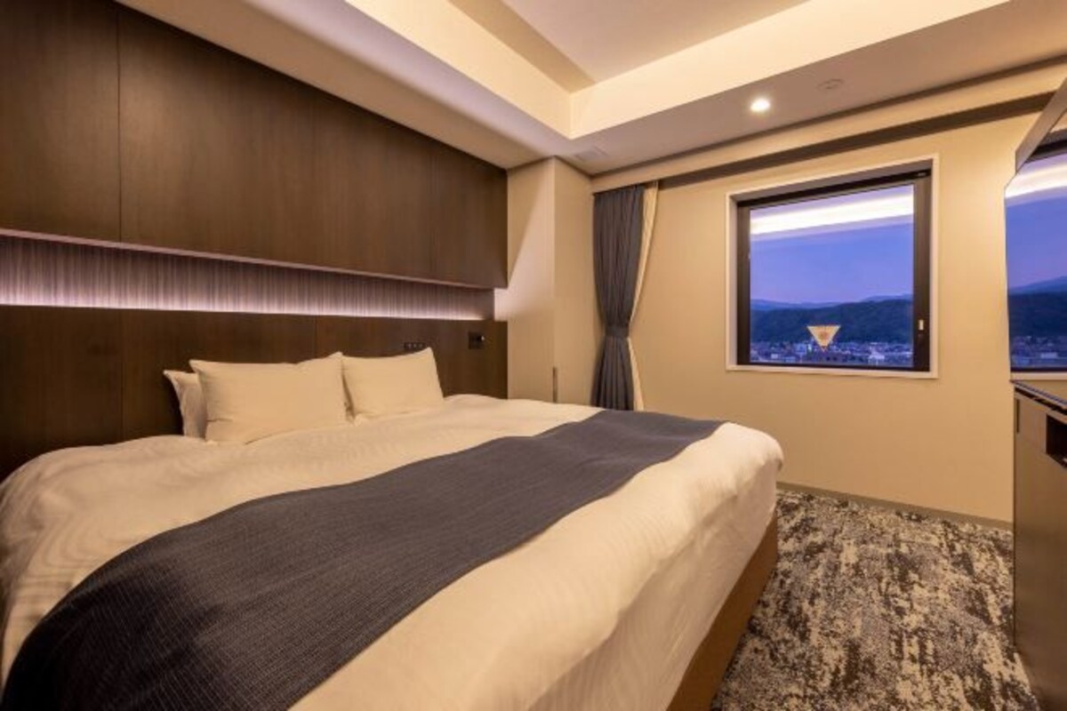 Ein Hotelzimmer mit einem großen Bett, Blick auf die Stadt durch ein Fenster und modernem Design.