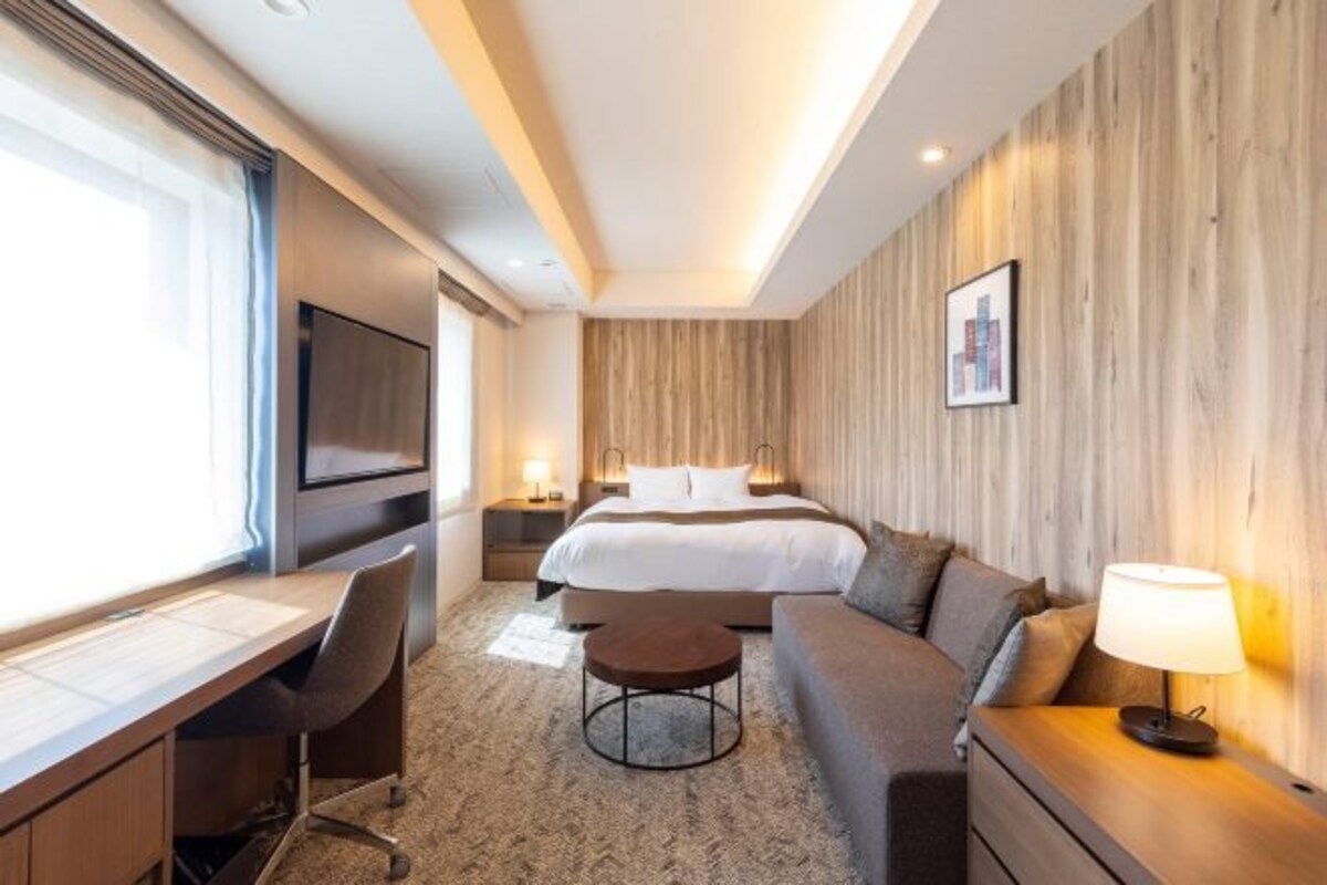 Ein Hotelzimmer mit Bett, Schreibtisch, Sessel, Sofa und Fernseher.