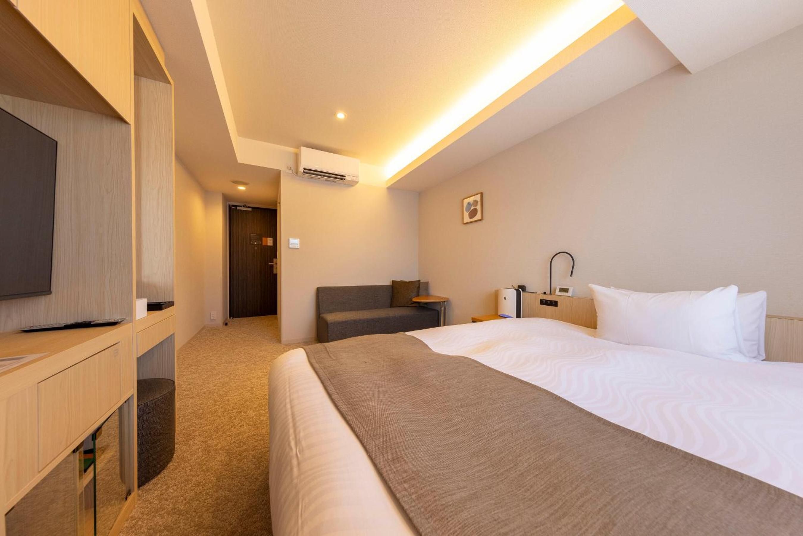 A hotel room with a bed, bedside table, lamp, and a television on a stand.