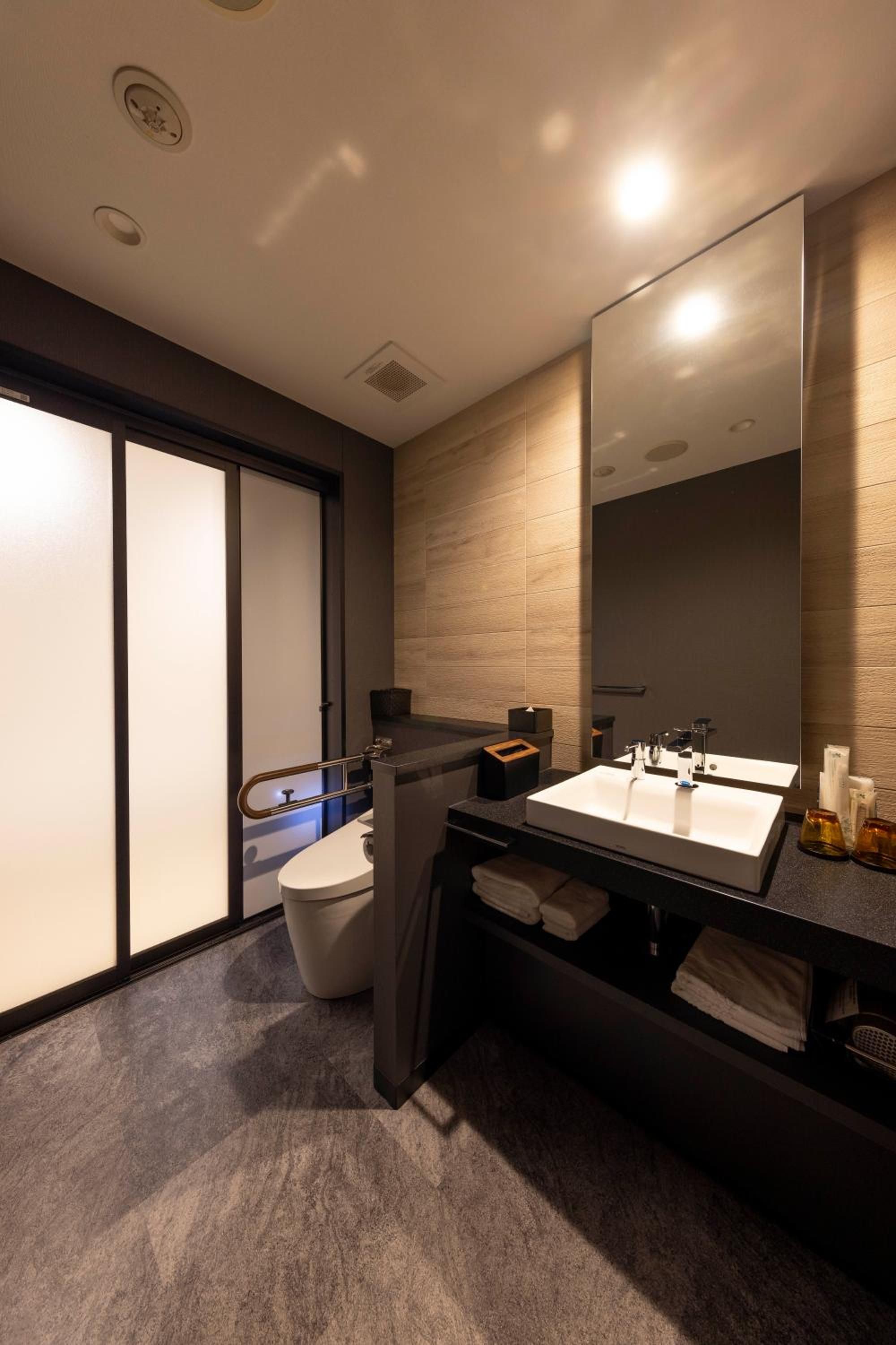 Un baño moderno con un espejo grande, un inodoro y un lavabo.