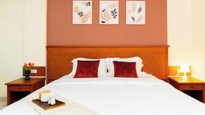 Ein ordentlich bezogenes Bett mit weißen und roten Kissen, ein Tablett mit Kerzen und einer Blumenvase sowie ein Kunstwerk an der Wand.
