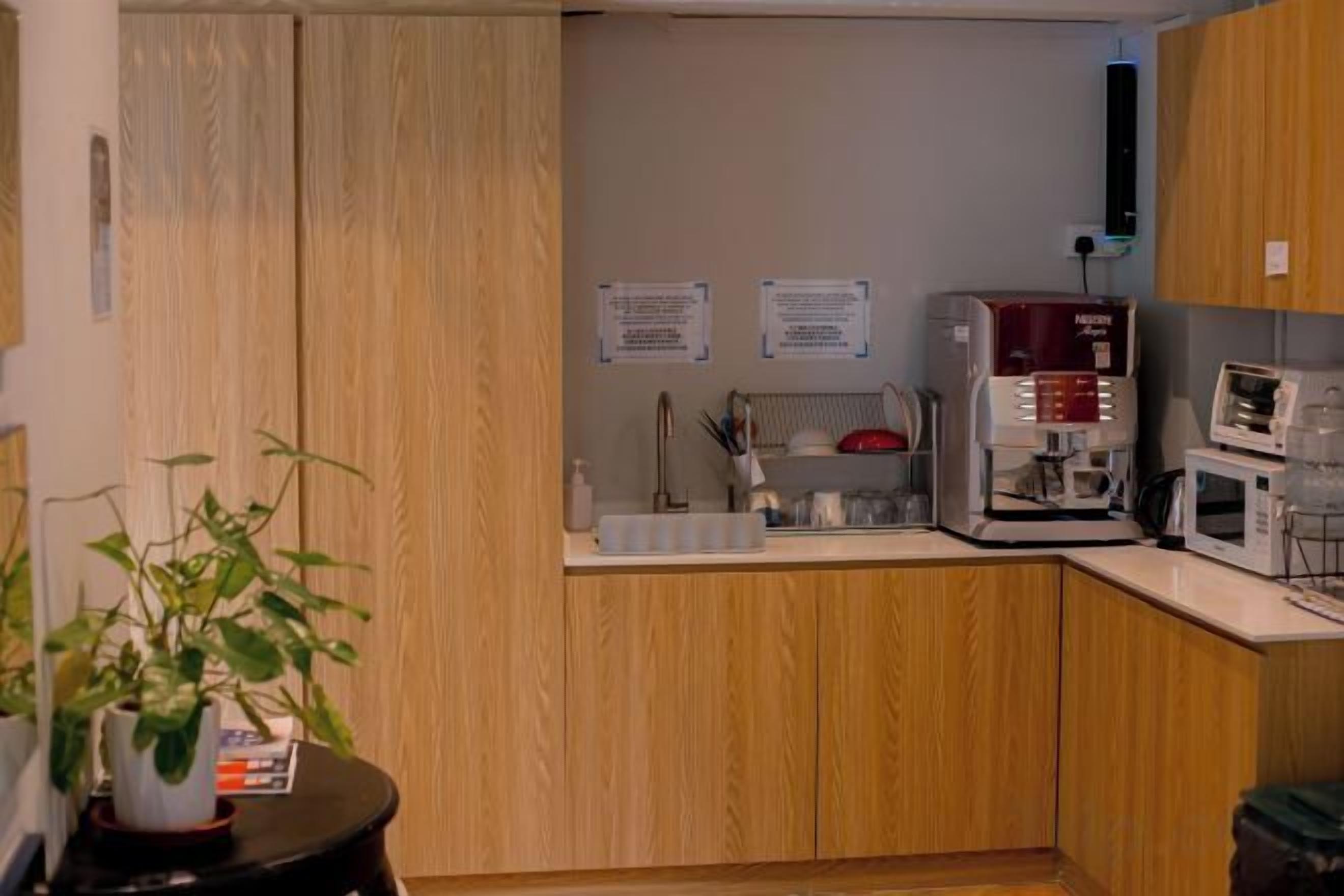 Una pequeña kitchenette equipada con microondas, cafetera y pileta. Hay muebles de madera y una planta en maceta.