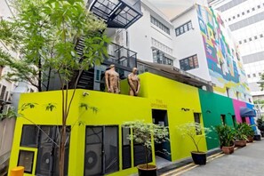 Un edificio de varios pisos con una fachada amarillo brillante, una escalera y un mural colorido en el edificio contiguo.