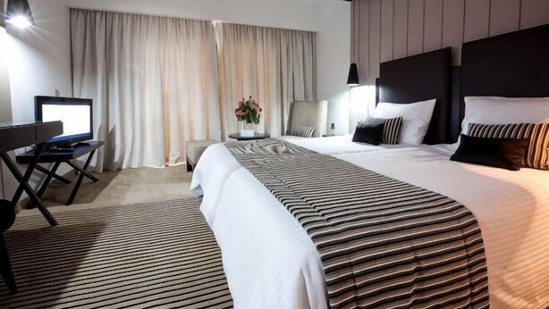A hotel room with a large bed, a desk with a computer, a chair, and a window with curtains. - El Mouradi Palace - Families and Couples Only (Akouda)