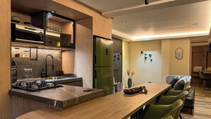 Cozinha moderna com ilha central, eletrodomésticos embutidos e área de refeições com cadeiras verdes.