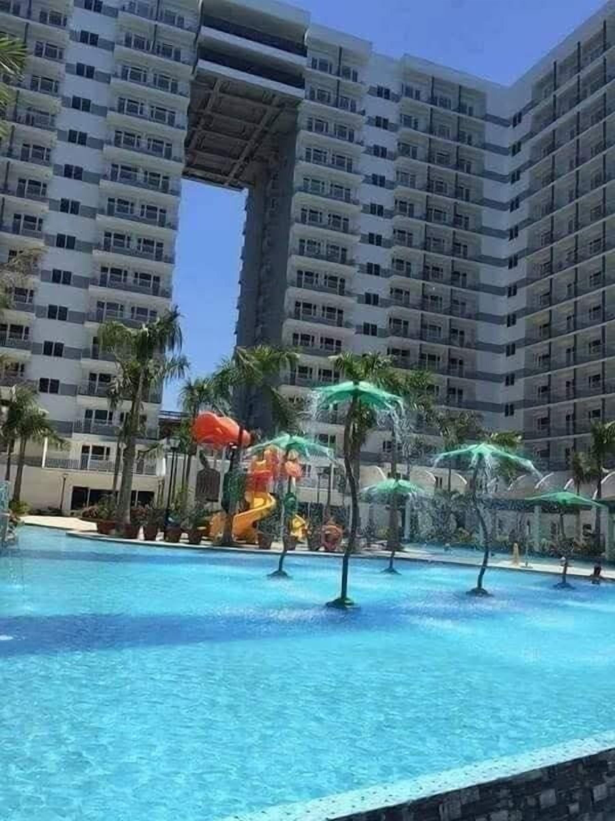 A hotel with a large swimming pool, palm trees, and a water slide.