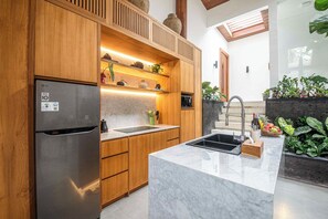 A modern kitchen with wooden cabinetry, a stainless steel refrigerator, a built-in oven, and a marble countertop.