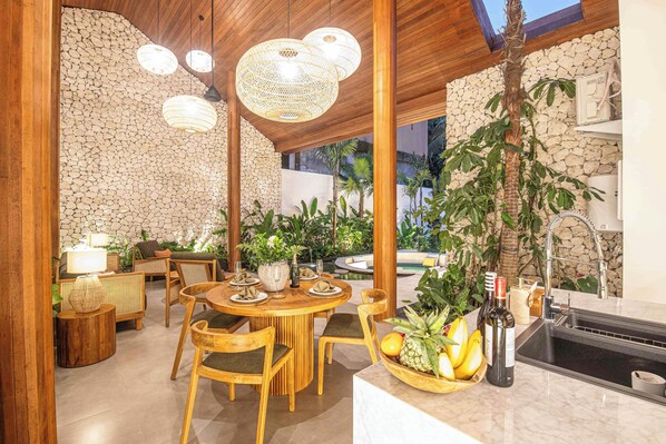 A dining area with a stone wall, wooden furniture, and hanging lights.