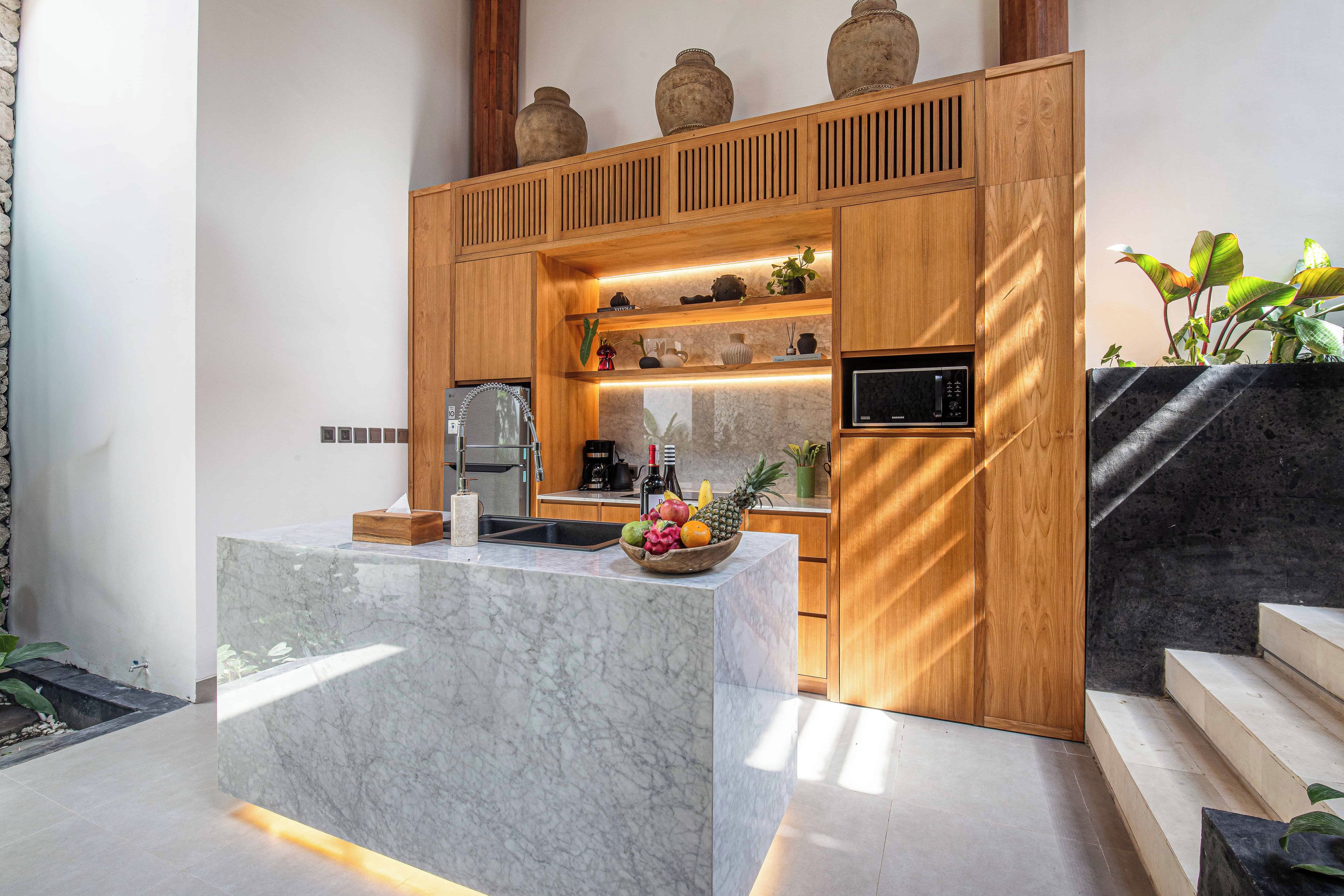 A modern kitchen with marble countertops, wooden cabinetry, and a fruit bowl.