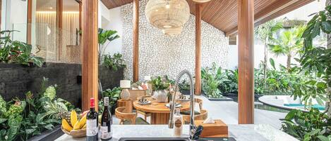 A modern kitchen with a stone backsplash, wooden ceiling, and a dining area with a round table and chairs.