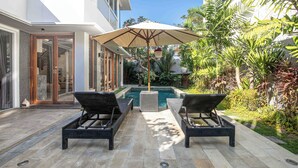 A modern outdoor pool area with two lounge chairs and a large umbrella. - Elegant 3BR Oasis in the Heart of Seminyak (Seminyak)