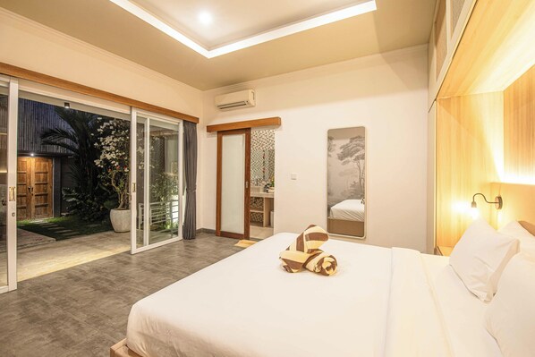 A modern bedroom with a large bed, a sliding glass door to a balcony, and a small bedside table with a lamp. - Elegant 3BR Oasis in the Heart of Seminyak (Seminyak)