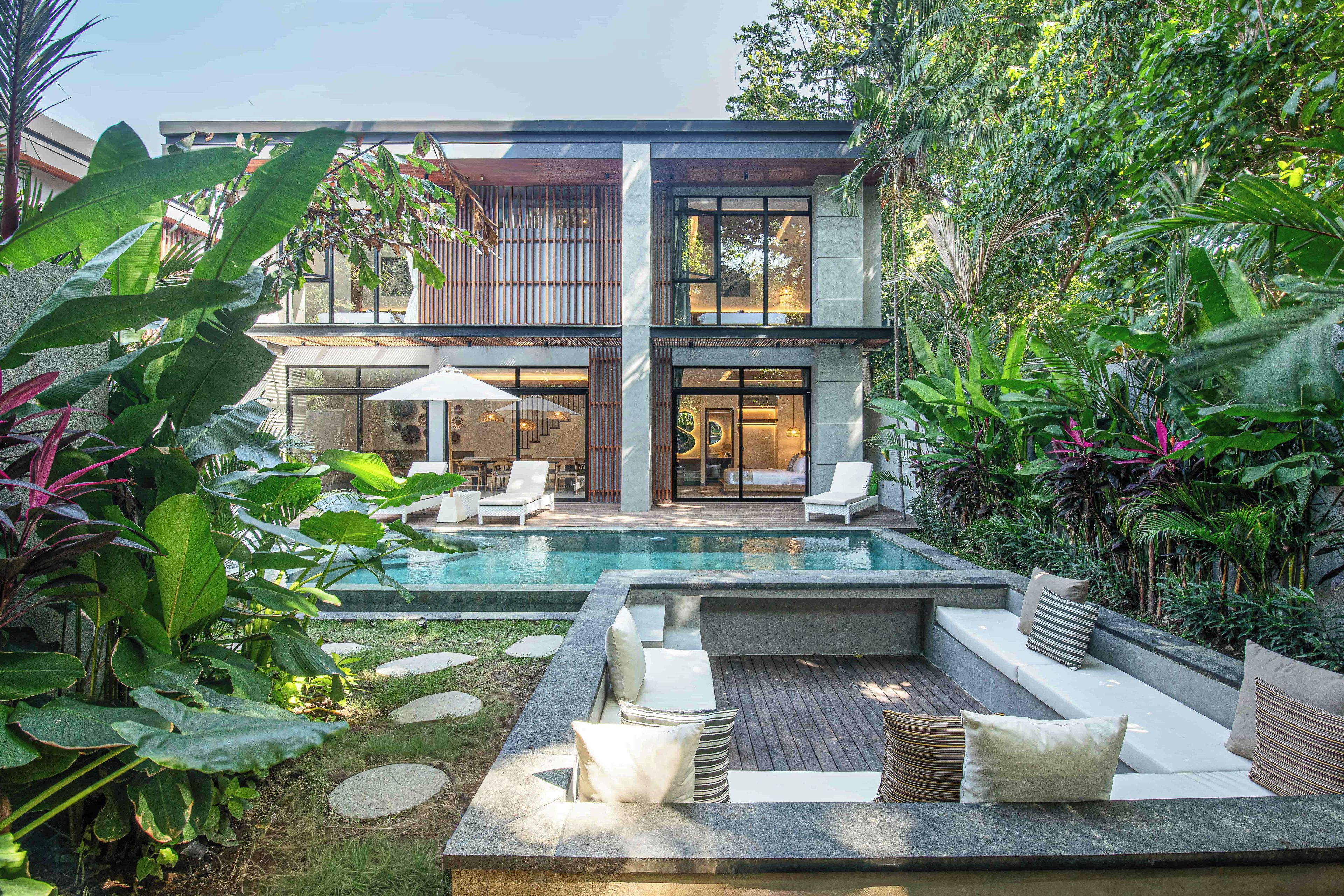 A modern two-story house with a swimming pool, outdoor seating area, and lush greenery.