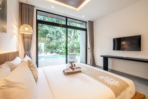 A modern hotel room with a large bed, a television, and a view of a swimming pool. - Stylish 5BR Designer Villa, 400m to the Ocean (Seminyak)