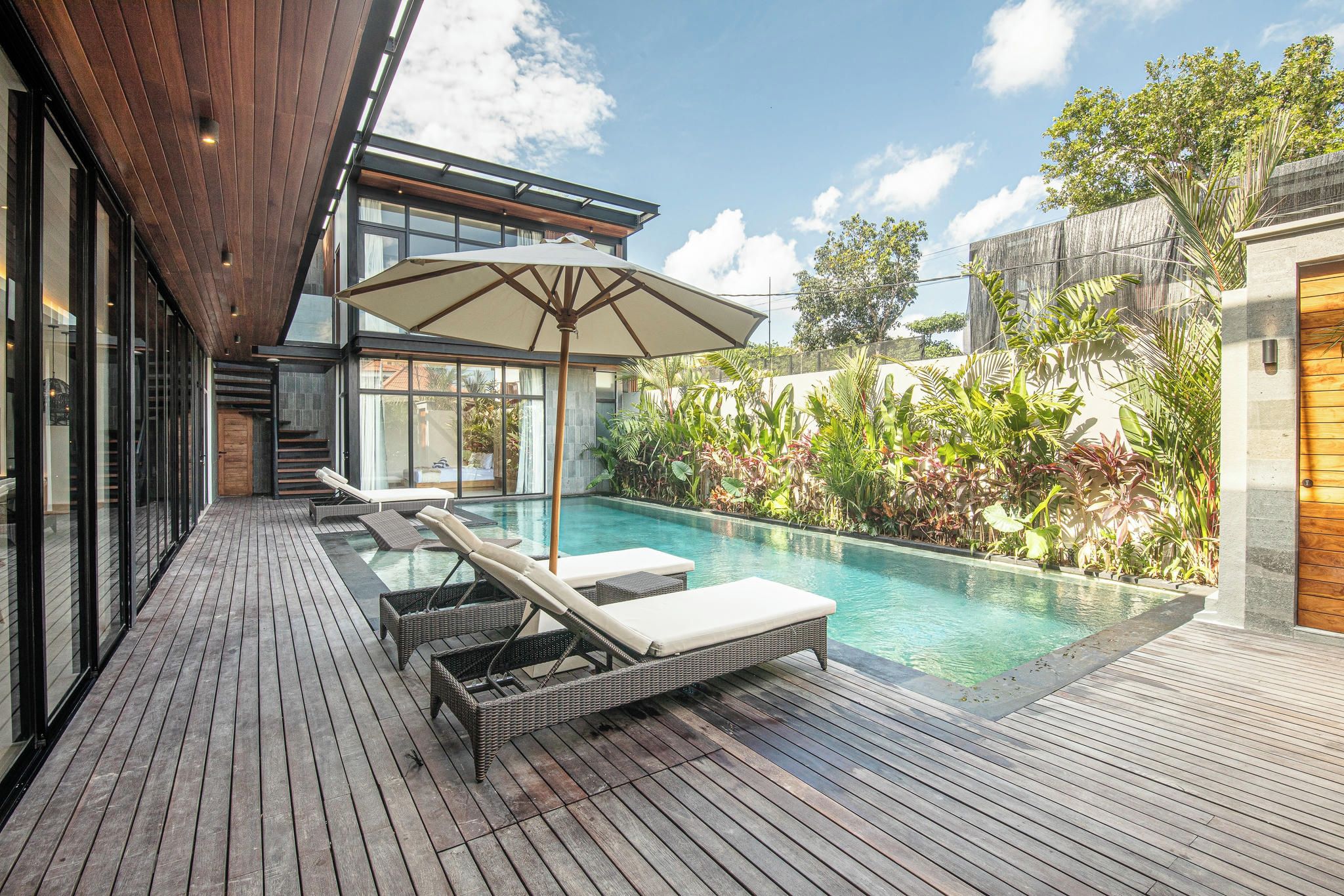 A modern outdoor pool area with lounge chairs and a large umbrella.