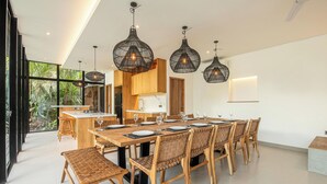 A modern dining area with a long wooden table set for six, surrounded by wicker chairs.