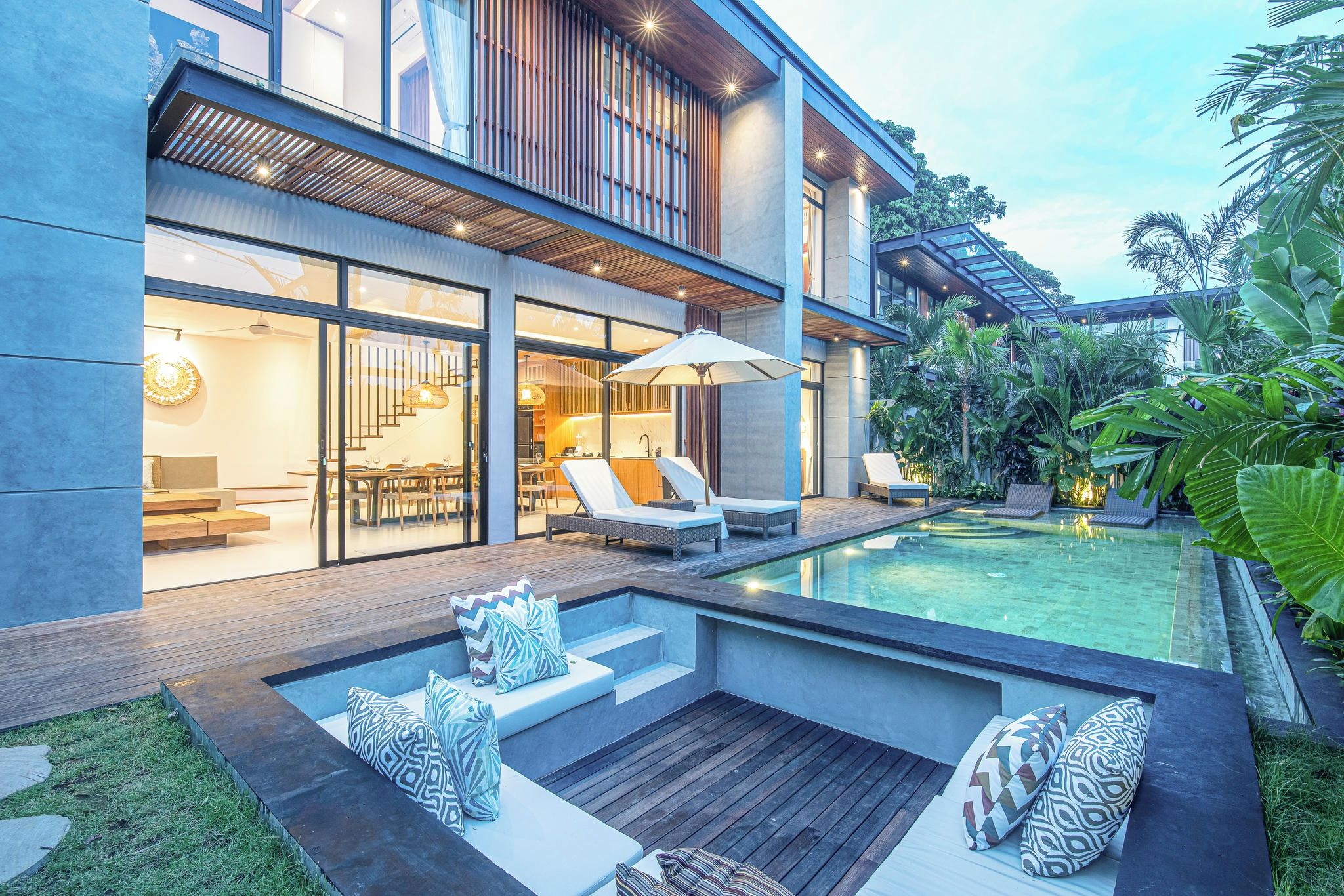 Een modern huis met een zwembad, terras en weelderige begroeiing.