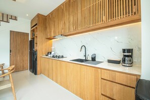 A modern kitchen with wooden cabinetry, a marble countertop, a sink, a coffee maker, and a built-in stove. - Elegant 5BR Modern Villa Steps From Café Del Mar (Seminyak)