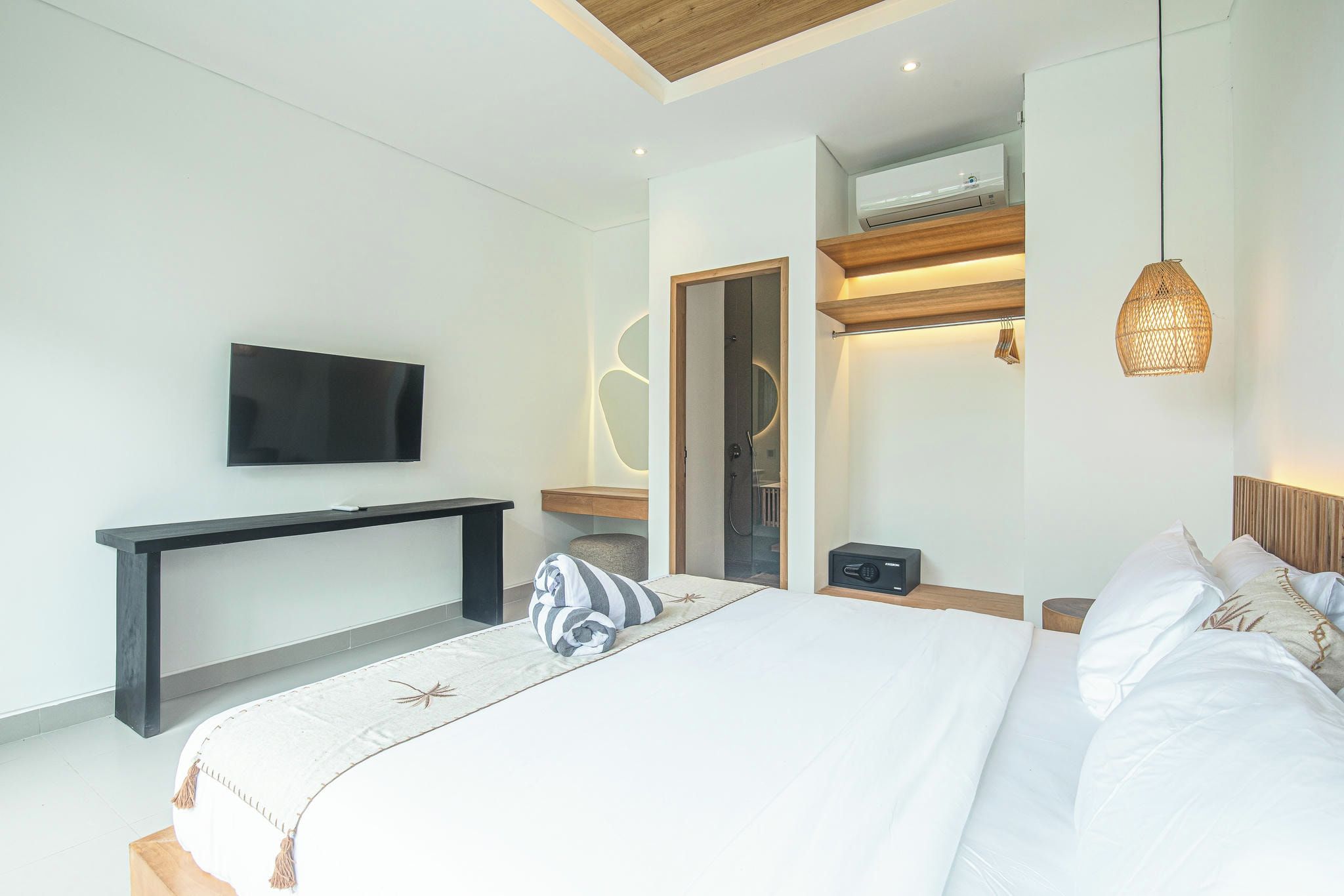 Un dormitorio moderno con una cama grande, un televisor de pantalla plana en la pared, una mesita de noche con lámpara y un equipo de aire acondicionado integrado.