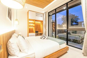Une chambre moderne avec un grand lit, une tête de lit en bois, une table de chevet et une grande fenêtre donnant sur l’extérieur.