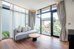 A modern living room with a grey sofa, a round wooden coffee table, and large windows with curtains. - Tropical Luxury 6BR Canggu Escape Near the Ocean (Seminyak)