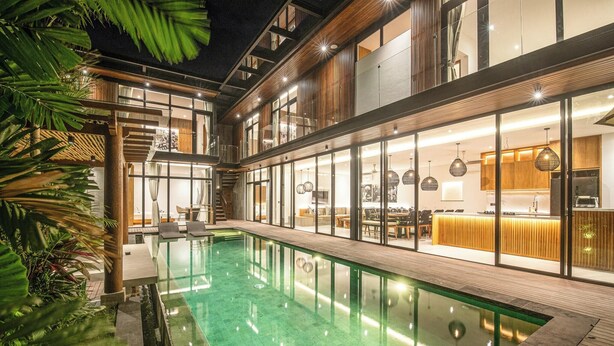 A modern hotel with a large indoor pool, wooden deck, and glass-enclosed rooms. - Tropical Luxury 6BR Canggu Escape Near the Ocean (Seminyak)