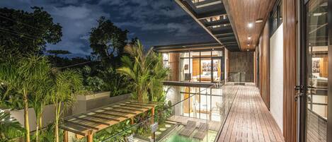 A modern house with a glass-enclosed pool, wooden deck, and a balcony overlooking the pool.
