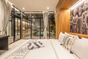 A modern hotel room with a large bed, a view of an indoor pool, and a wooden wall with a framed picture. - Tropical Luxury 6BR Canggu Escape Near the Ocean (Seminyak)