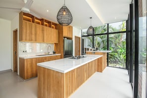 A modern kitchen with wooden cabinets, a large island, and pendant lighting. - Tropical Luxury 6BR Canggu Escape Near the Ocean (Seminyak)