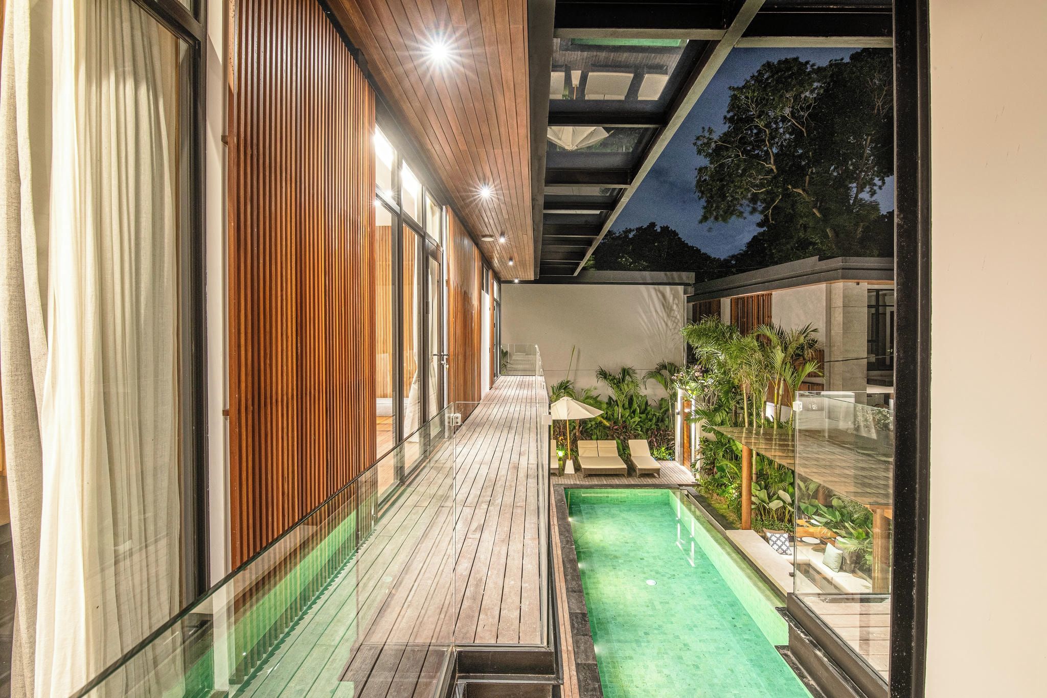 A modern building with a wooden deck, a swimming pool, and glass railings.