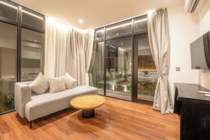 A modern living room with a sofa, a round coffee table, and a large window with curtains. - Tropical Luxury 6BR Canggu Escape Near the Ocean (Seminyak)