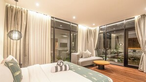 A modern hotel room with a large bed, a sofa, a small table, and a view through large glass doors. - Tropical Luxury 6BR Canggu Escape Near the Ocean (Seminyak)
