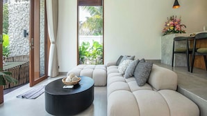 Uma sala de estar moderna com um sofá bege, uma mesa de centro redonda preta e uma parede de pedra.