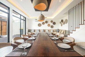 Un espace de salle à manger moderne, avec une longue table en bois, plusieurs chaises et un luminaire suspendu au centre.