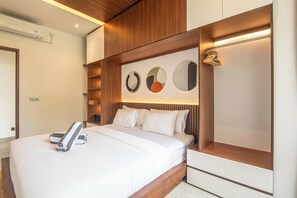 A modern hotel room with a large bed, wooden headboard, and a wall-mounted shelf with decorative plates. - Luxury 5BR Villa in Canggu, Walk to the Beach (Canggu)