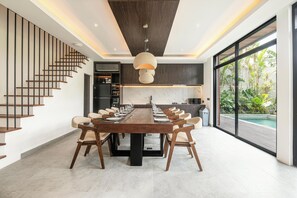 A modern dining area with a long wooden table, multiple chairs, and a staircase on the left. - Luxury 5BR Villa in Canggu, Walk to the Beach (Canggu)