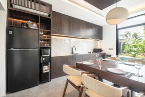 A modern kitchen with dark cabinetry, a built-in refrigerator, and a dining area with a table and chairs. - Luxury 5BR Villa in Canggu, Walk to the Beach (Canggu)