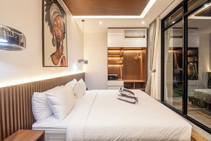 Una habitación de hotel moderna con una cama grande, cabecera de madera, un cuadro en la pared y una puerta corrediza de vidrio que da a un balcón.